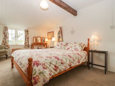 A bedroom with a wooden bed and floral bedding a dressing table and a window with floral curtains at Church Farmhouse in Winsham
