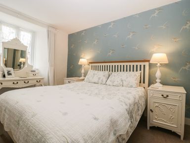 A bedroom with a bed with floral bedding two bedside tables with lamps a dressing table with mirror and a window at Church Farmhouse in Winsham