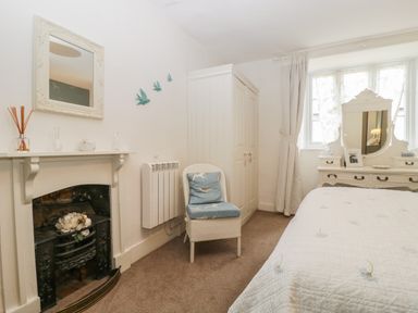 A bedroom with a bed a chair a wardrobe a dresser with mirror and a non-working fireplace at Church Farmhouse in Winsham