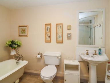 A bathroom with a bathtub flowers toilet sink and a mirror at Church Farmhouse in Winsham