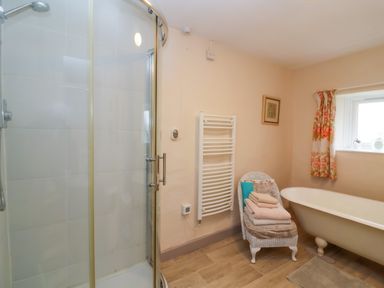 A bathroom with a corner shower enclosure a white heated towel rail a white clawfoot bathtub and a chair with folded towels at Church Farmhouse in Winsham