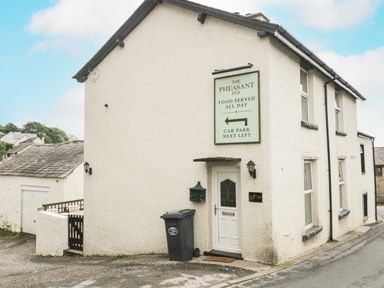 Exterior of a white building with a door and a sign for The Pheasant Inn in a small village
