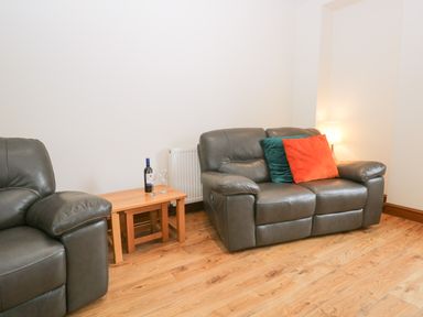 A living room with two leather sofas a wooden side table with a bottle of wine and two glasses at Fernleigh Cottage in Allithwaite near Grange-over-Sands