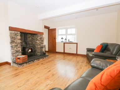 A living room with a stone fireplace wooden floor brown door leather sofas and colorful cushions at Fernleigh Cottage in Allithwaite near Grange-over-Sands