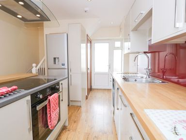 A kitchen with wooden countertops a sink a refrigerator an oven and a white door at Fernleigh Cottage in Allithwaite near Grange-over-Sands