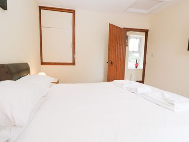 A bedroom with a bed made with white sheets and towels on top a wooden door and a window with a red vase on the sill Fernleigh Cottage Allithwaite near Grange-over-Sands