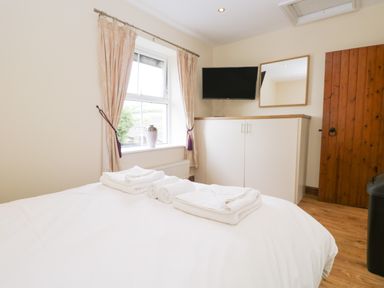 A bedroom with a bed towels on a cabinet window and a wooden door at Fernleigh Cottage in Allithwaite near Grange-over-Sands