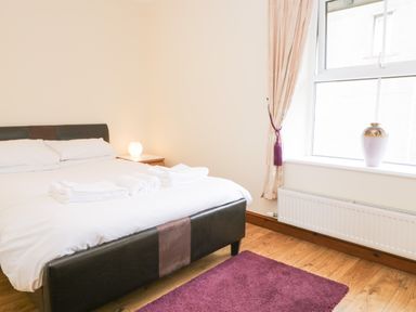A bedroom with a bed with white sheets and towels bedside lamp purple rug and window with curtain at Fernleigh Cottage in Allithwaite near Grange-over-Sands
