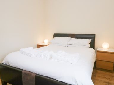 A bedroom with a double bed white bedding and folded towels on it with two bedside tables and lamps at Fernleigh Cottage in Allithwaite near Grange over Sands