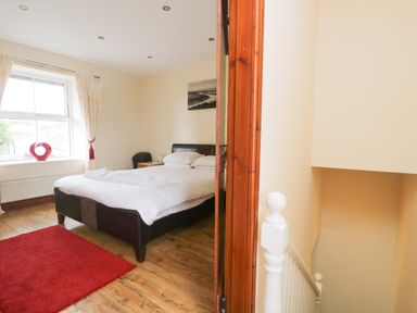 A bedroom with a double bed white linens red rug and a window near stairs at Fernleigh Cottage in Allithwaite near Grange over Sands