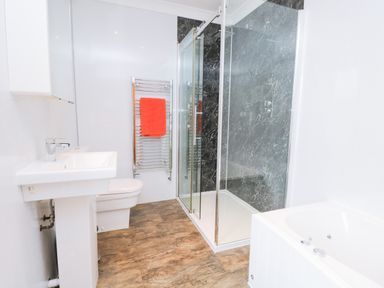 A bathroom with a white sink toilet bathtub glass shower enclosure and a towel rack with an orange towel at Fernleigh Cottage in Allithwaite near Grange-over-Sands