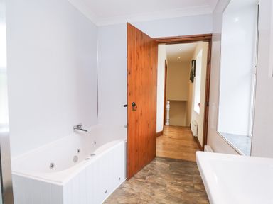 A bathroom with a bathtub sink wooden door and view of hallway at Fernleigh Cottage in Allithwaite near Grange-over-Sands