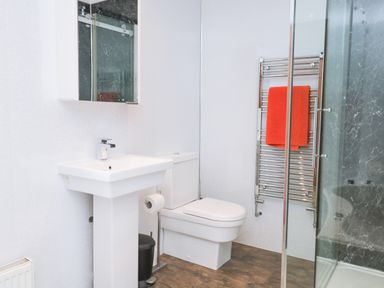 A bathroom with a pedestal sink toilet glass shower and a towel rack with a red towel at Fernleigh Cottage in Allithwaite near Grange-over-Sands