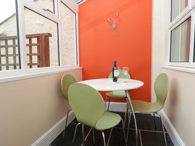 A dining area with green chairs around a white round table with wine bottle and glasses against an orange wall at Fernleigh Cottage in Allithwaite near Grange-over-Sands