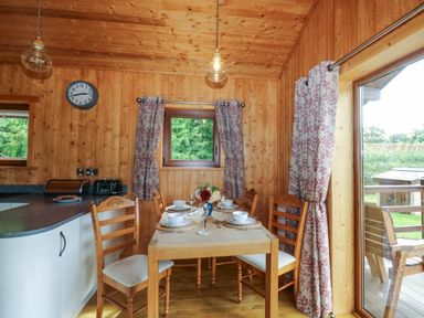 A wooden dining area with a table set for four near a kitchen countertop and large window at Barn Shelley Lodge in Copplestone near Crediton