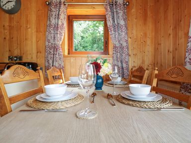 A dining table set with white bowls and plates glasses cutlery and a flower vase in a wooden room at Barn Shelley Lodge Copplestone near Crediton