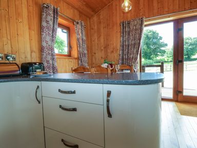 A kitchen area with white cabinets a countertop and a dining table with chairs near windows and glass doors at Barn Shelley Lodge Copplestone near Crediton