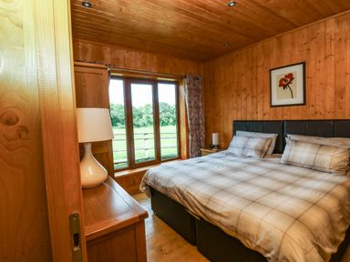 A bedroom with a double bed next to a window and wooden walls at Barn Shelley Lodge in Copplestone near Crediton