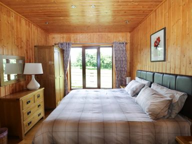 A bedroom with a large bed dresser with lamp wardrobe and glass doors at Barn Shelley Lodge Copplestone near Crediton