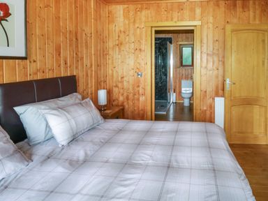 A bedroom with a bed a bedside table and a lamp and a doorway leading to a bathroom at Barn Shelley Lodge in Copplestone near Crediton