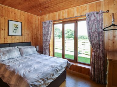 A bedroom with a double bed next to a window with curtains and a wooden dresser at Barn Shelley Lodge in Copplestone near Crediton