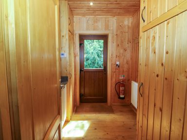 A wooden hallway with a door at the end and wardrobes on both sides at Barn Shelley Lodge in Copplestone near Crediton