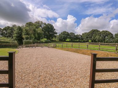 A gravel driveway with wooden fences and green fields beyond under a partly cloudy sky at Barn Shelley Lodge Copplestone near Crediton