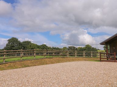 An outdoor area with wooden fencing grass and a gravel surface next to a building at Barn Shelley Lodge in Copplestone near Crediton