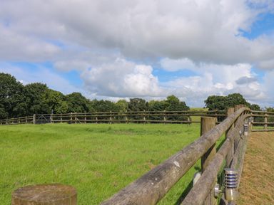 A green field enclosed by wooden fences with trees in the background at Barn Shelley Lodge in Copplestone near Crediton