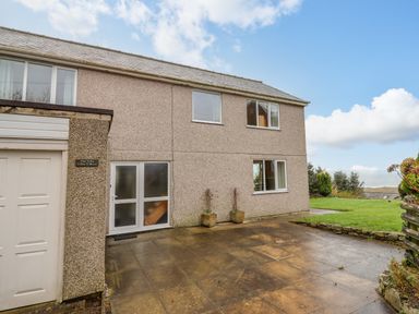 Exterior of a two-story house with windows a garage door and a paved driveway with grass and shrubs at The Villa in Harlech