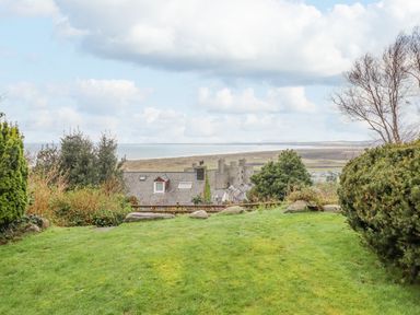 A grassy garden with bushes and trees overlooking rooftops and a castle with a coastline in the background at The Villa in Harlech
