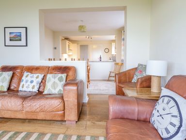A living room with brown leather sofas and pillows and a wooden side table with a lamp at The Villa in Harlech