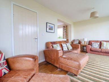 A living room with brown leather sofas cushions a wooden side table lamp and a striped rug at The Villa in Harlech