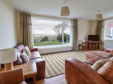 A living room with leather sofas striped rug wooden side tables lamps and a large window with a view at The Villa in Harlech