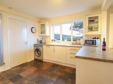 A kitchen with white cabinets a washing machine a microwave and a window with a view at The Villa in Harlech