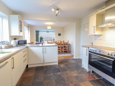 A kitchen with white cabinets and appliances opening to a dining area with wooden chairs at The Villa in Harlech