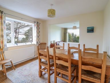 A dining room with a wooden table and chairs next to a window with patterned curtains at The Villa in Harlech