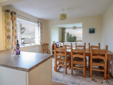 A dining room with a wooden table and chairs next to large windows at The Villa in Harlech