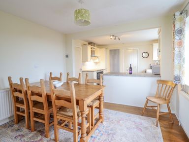 A dining area with a wooden table and six chairs next to a kitchen with countertops and cabinets at The Villa in Harlech