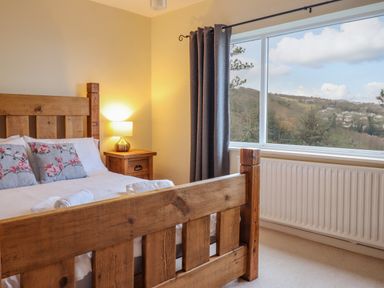 A bedroom with a wooden bed frame side table with lamp and large window showing hillside view at The Villa in Harlech