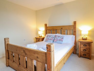 A bedroom with a wooden bed frame two bedside tables with lamps and decorative cushions on the bed at The Villa in Harlech