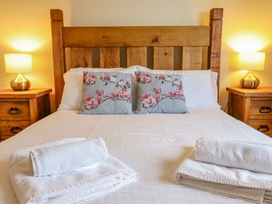A bed with wooden headboard two floral pillows and two bedside tables with lamps at The Villa in Harlech