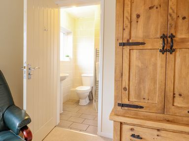 A bathroom with a toilet sink and towel rack visible through an open door from a room with a wooden cabinet and green chair at The Villa in Harlech