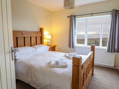 A bedroom with a wooden bed a bedside table with a lamp and a window with a view at The Villa in Harlech