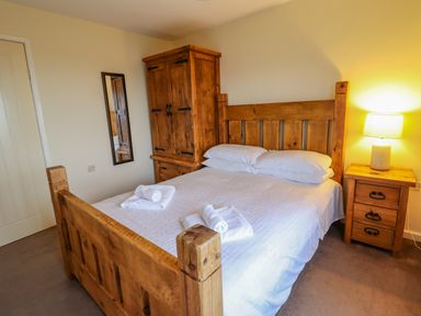 A bedroom with a wooden bed frame bedside table with lamp wooden wardrobe and mirror on the wall at The Villa in Harlech