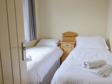 A small bedroom with two single beds a wooden nightstand and folded towels at The Villa in Harlech