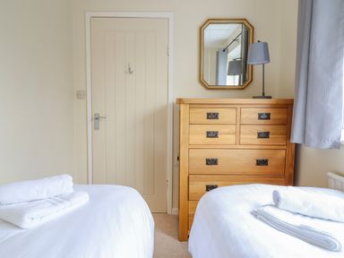 A bedroom with two beds with towels on them a wooden chest of drawers a mirror a lamp and a door at The Villa in Harlech