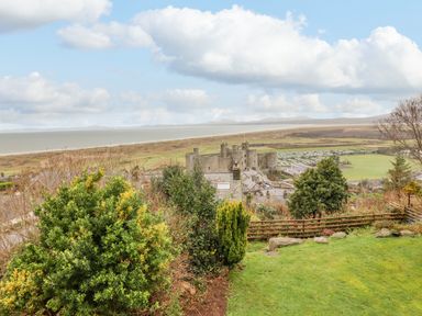 A garden with bushes and a wooden fence overlooking a castle near the coast with fields in the background at The Villa in Harlech