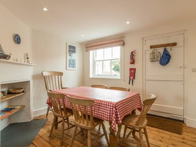 A dining room with a table covered by a red and white checkered tablecloth and six wooden chairs at 3B Coastguard Cottages in Low Newton-By-The-Sea