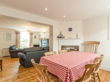 A dining room with wooden chairs and a table covered with a red and white checkered cloth connecting to a living room with two sofas and a window at 3B Coastguard Cottages in Low Newton-By-The-Sea